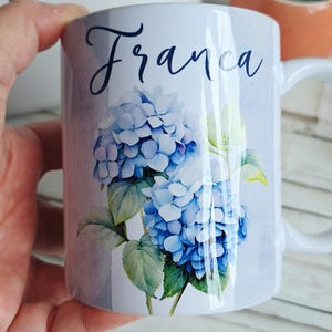 Può includere: Tazza in ceramica bianca con un motivo floreale di ortensie blu e il nome "Franca" in corsivo. La tazza ha un manico bianco ed è adatta per bevande calde o fredde. Un bel regalo per Franca.