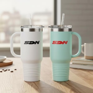Puede incluir: Dos tazas de viaje aisladas con asas y pajitas. Una es blanca con texto negro "SDN", la otra es verde azulado claro con texto rojo "SDN". Ambas tienen bordes y tapas plateadas.