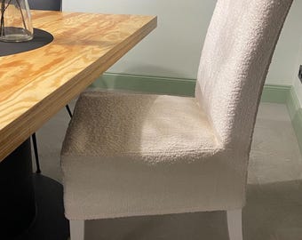 Könnte beinhalten: Ein weißer, flauschiger Stuhl mit einem Holzrahmen und Beinen. Der Stuhl steht neben einem Holztisch.