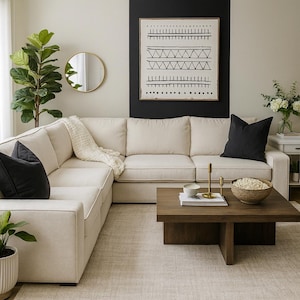 May include: A cream-colored sectional sofa with two black throw pillows and a white textured throw blanket. A square wooden coffee table sits in front, holding a bowl of popcorn, a small white bowl, and two gold-toned candle holders.