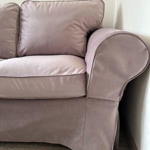Può includere: Una sezione di un divano color malva con un bracciolo arrotondato e un grande cuscino morbido. Il divano ha una base a gonna e un cuscino schienale abbinato. Il tessuto sembra essere un morbido velluto.