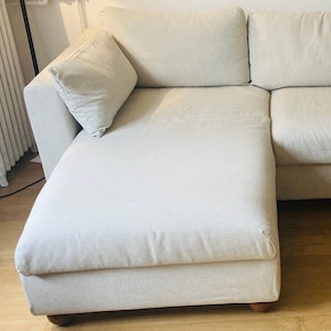May include: A white sectional sofa with a chaise lounge. The sofa has a light gray fabric upholstery and a simple design.