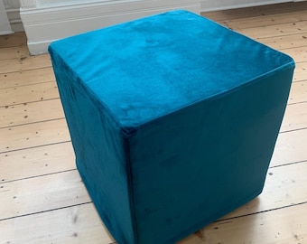 Pode incluir: Um pufe quadrado azul turquesa com uma capa de tecido macio e felpudo.