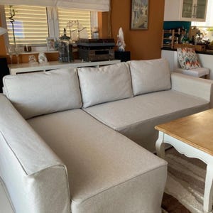 May include: A large, light grey sectional sofa with a chaise lounge. The sofa has three cushions and a white coffee table in front of it.