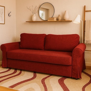 Könnte beinhalten: Ein rotes Sofa mit gerollten Armlehnen und einem gerüschten Sockel steht auf einem gemusterten Teppich. Das Sofa ist der Mittelpunkt eines Wohnzimmers, mit einem runden Spiegel und einem dekorativen Regal im Hintergrund.