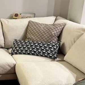 May include: A beige sectional sofa with three cushions. The cushions are patterned with black and white circles, brown and white circles, and a floral design. The sofa is in a living room setting.