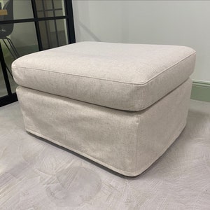 May include: A light beige fabric ottoman with a tufted top. The ottoman has a square shape and is made of a soft, textured fabric.