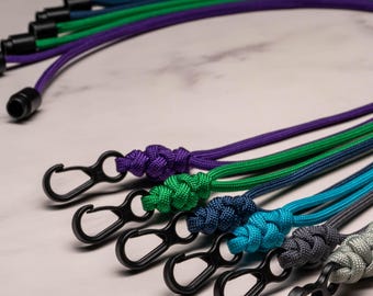May include: A set of colorful lanyard cords with black metal clasps. The cords are made of paracord and come in a variety of colors, including green, blue, purple, and gray.