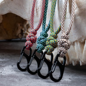 May include: Four colorful paracord keychains with black metal lobster clasps. The paracord is woven in a variety of patterns, including red and blue, teal and white, yellow and blue, and brown and white.