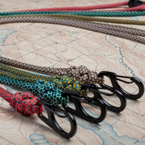 May include: Five colorful patterned ropes with black metal clips attached. The ropes are arranged in a semi-circle on a brown and white map.