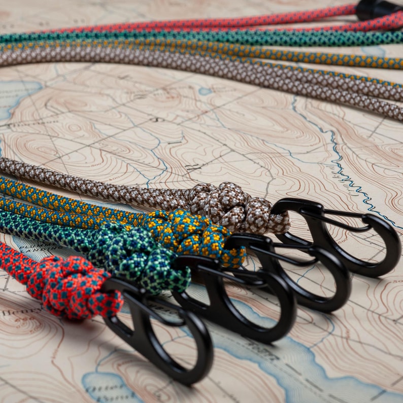 May include: Five colorful patterned ropes with black metal clips attached. The ropes are arranged in a semi-circle on a brown and white map.
