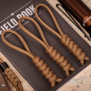 May include: Three brown paracord keychains with a braided knot design. The keychains are on a map background.