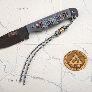 May include: A black and grey pocket knife with a black and grey paracord lanyard and a bronze metal token with the text "EXTINCTION LEVEL EVENT ELE SURVIVAL" on it.