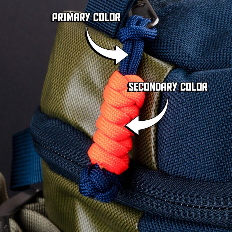 Puede incluir: Una mochila azul marino y verde oliva con un tirador de cremallera de paracord. El tirador consiste en un lazo de cord&oacute;n azul oscuro con una secci&oacute;n trenzada de color naranja brillante y un nudo azul oscuro en el extremo.