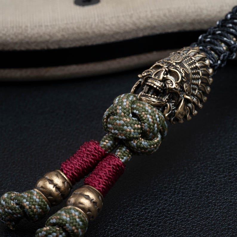 May include: A green, black, and red paracord bracelet with a brass skull bead. The skull bead has intricate details and a fierce expression.