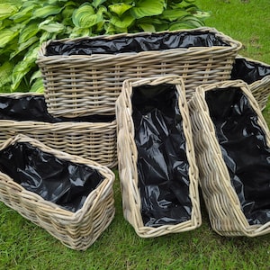 May include: Set of six wicker planters in various sizes, with black plastic liners. The planters are arranged on a green grassy surface.
