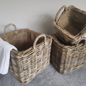 May include: Three grey wicker baskets with fabric liners. The baskets are square and have two handles on each side. The baskets are stacked on top of each other.