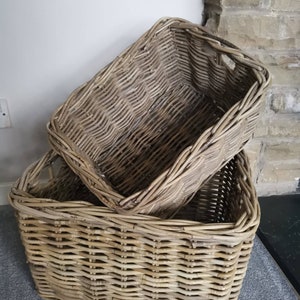 May include: Two woven wicker baskets, one stacked on top of the other. The top basket is rectangular and the bottom basket is square. Both baskets are made of natural woven wicker.