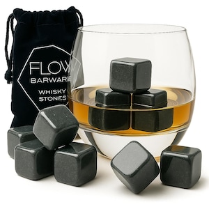 May include: A collection of dark grey whisky stones, some in a glass of amber liquid, and others scattered around. A black drawstring bag with the text "FLOW BARWARE WHISKY STONES" is visible. The stones are cube-shaped.
