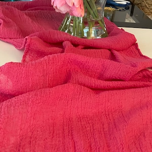 May include: A pink textured table runner with a ruffled edge. The runner is made of a soft, lightweight fabric and is perfect for adding a touch of elegance to any table setting.