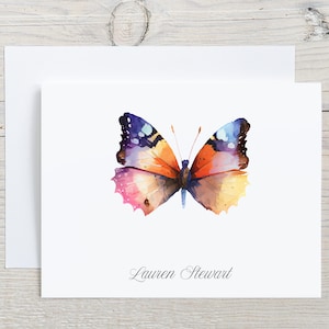 May include: A watercolor painting of a butterfly with orange, pink, yellow, and purple wings. The butterfly is on a white background with the name "Lauren Stewart" written in cursive below it.