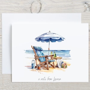 May include: Watercolor illustration of a beach scene on a white card. A blue and white striped beach chair sits under a blue umbrella. A small table holds bottles and a newspaper. The text "a note from Lauren" is at the bottom.
