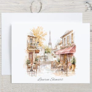 May include: Watercolor illustration of a Parisian street scene with the Eiffel Tower in the background. The image features cafes with tables and chairs, a fountain, and the text "Paris". The name "Lauren Stewart" is written at the bottom.