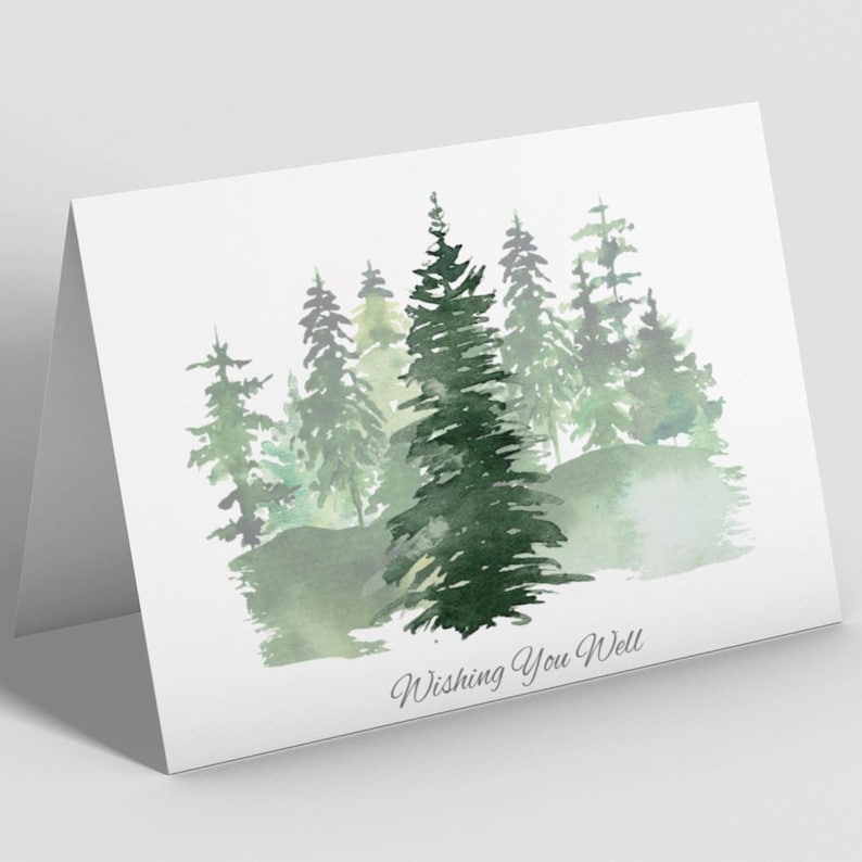 Puede incluir: Una tarjeta de felicitaci&oacute;n plegada con una ilustraci&oacute;n de acuarela de una escena de bosque. La imagen presenta varios pinos verdes y el texto "Wishing You Well" en una fuente cursiva. La tarjeta es blanca.