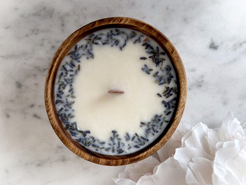 May include: A white candle with dried lavender flowers embedded in the wax. The candle is in a wooden bowl.