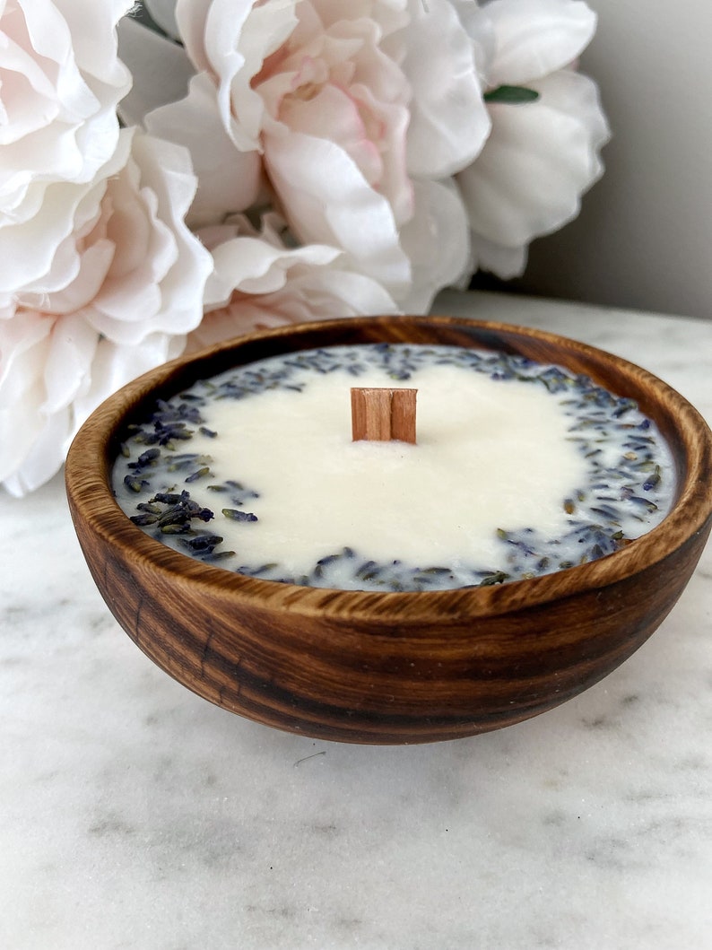 May include: A wooden bowl candle with a white wax top and a wooden wick. The wax is infused with dried lavender flowers.