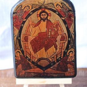 May include: A wooden icon depicting Jesus Christ seated on a throne with four angels surrounding him. The icon is painted in a traditional style with vibrant colors and gold accents. The background is a dark brown wood.