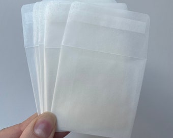 May include: A stack of five white, translucent, plastic sleeves with a clear, rectangular window in the center.