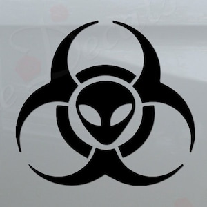 May include: Black and white alien head inside a biohazard symbol decal. The decal is on the back of a white pickup truck.