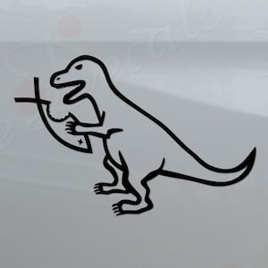 May include: Black and white vinyl decal of a dinosaur holding a cross. The decal is applied to the back of a white pickup truck. The truck has a black bumper with the words "Rosie Decals" in red letters.