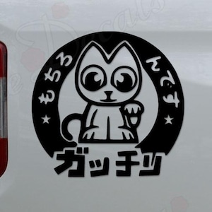 May include: Black and white cat decal with Japanese text. The cat has large eyes and is inside a circular frame. The decal is affixed to the side of a white vehicle.