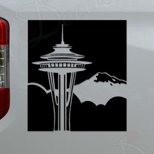 May include: A black and white square decal featuring the Space Needle and a mountain range. The decal is affixed to the side of a white truck. The Space Needle is a prominent landmark in Seattle, Washington.