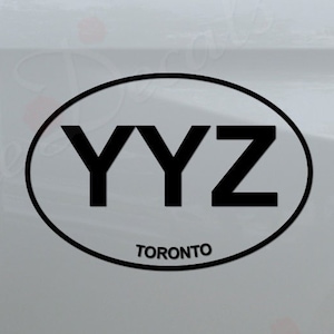 May include: Black and white oval sticker with the text "YYZ TORONTO" on a white truck tailgate.