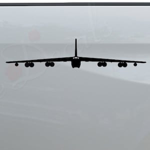 May include: A black silhouette of a B-52 bomber plane decal on the back of a white pickup truck. The decal is on the driver's side of the truck. The truck has a chrome bumper with the words "Rosie Decals" in black lettering.