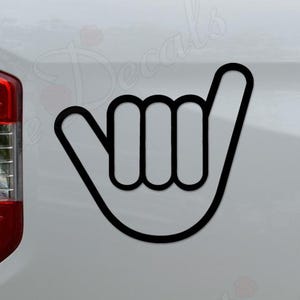 May include: Black outline of a hand in the shaka sign, a gesture of friendship and understanding. The decal is affixed to the white side of a truck. The truck's taillight is visible on the left side of the image.