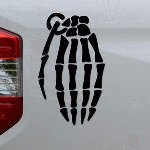 May include: Black decal of a skeleton hand grenade applied to the side of a white vehicle. The graphic is a detailed illustration of a hand grenade with a skeletal hand holding the pin.