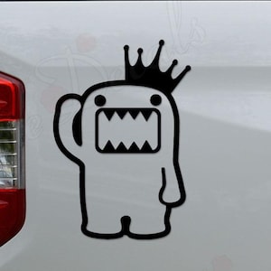 May include: A black and white vinyl decal featuring a cartoon monster with a crown. The monster has a large mouth with sharp teeth and is waving. The decal is applied to the side of a white vehicle.