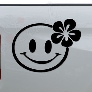 May include: Black and white smiley face decal with a flower on a white truck tailgate.