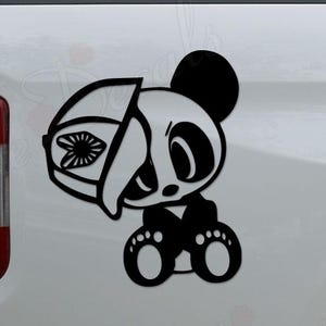 May include: Black and white panda bear sticker with a helmet design. The panda is wearing a helmet with a floral design on the visor. The sticker is applied to the side of a white vehicle.