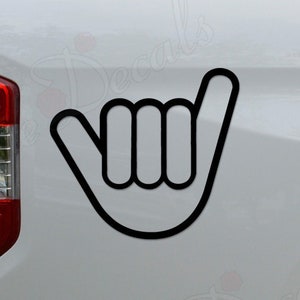 May include: Black outline of a shaka hand gesture sticker on a white vehicle. The sticker is placed on the side of the vehicle near the taillight. The shaka symbol is a hand gesture associated with surf culture.