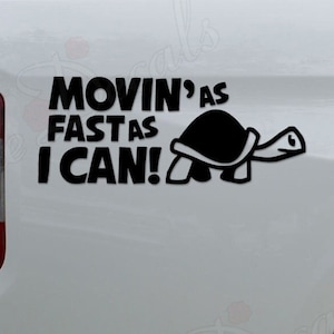 May include: A white pickup truck with a black decal on the back that says "Movin' as fast as I can!" with a cartoon turtle next to the text.