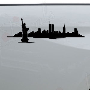 May include: Black silhouette decal of the New York City skyline, including the Statue of Liberty and the Twin Towers, on the back of a white pickup truck.