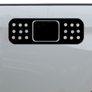 May include: A black and white vinyl decal of a bandage, designed to look like a real bandage. The decal is applied to the back of a white pickup truck.