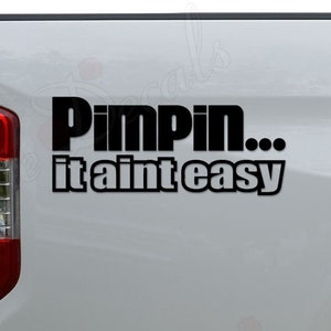 May include: A white pickup truck with a black vinyl decal that reads "Pimpin... it ain't easy".