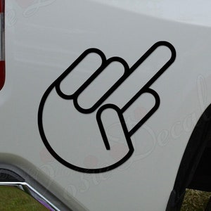 May include: Black and white decal of a hand giving the middle finger. The decal is applied to the back of a white pickup truck.