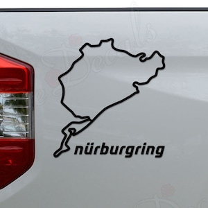 May include: A white pickup truck with a black vinyl decal of the Nürburgring race track on the back. The decal is outlined in black and includes the text "Nürburgring".